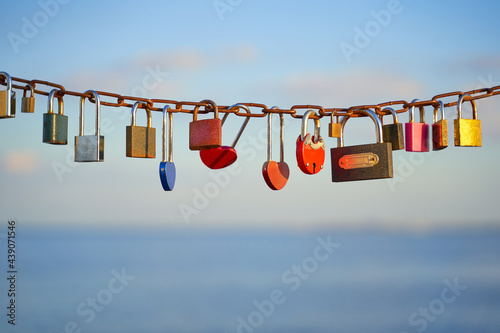 Various and heart colorful shaped love padlocks on a chain on a beautiful blue sky and sea background. Diverse locks as a symbol of togetherness and bonding.