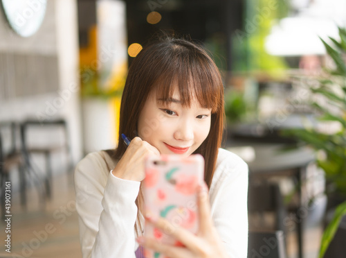 Young adult asian student woman using mobile phone for online application at indoor cafe.