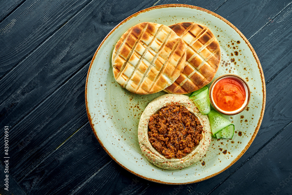A classic oriental dish - chickpea hummus with olive oil and minced meat served with baked pita in a plate on a dark wood background. Vegetarian food. Diet A classic oriental dish - chickpea hummus with olive oil and minced meat served with baked pita in a plate on a dark wood background. Vegetarian food. Diet