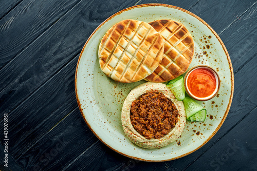 A classic oriental dish - chickpea hummus with olive oil and minced meat served with baked pita in a plate on a dark wood background. Vegetarian food. Diet
