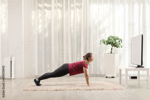 Young woman doing plank exercises in front of a tv