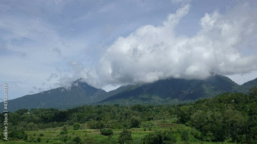 Timelapse of clouds moving from wind in blue sky on sunny day with a volcano on background. trees, tropical area
