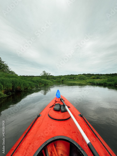 Kayaking on the river. View from the red kayak on the river shore in early summer season. Bow of red kayak. Kayaking on peaceful calm river