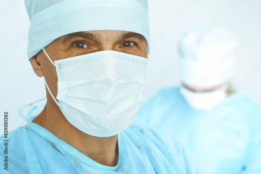 A male surgeon headshot, a group of surgeons is operating in the background. Health care concept A male surgeon headshot, a group of surgeons is operating in the background. Health care concept