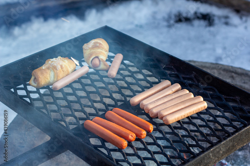Sausages and sausage buns on a barbecue grill over a fire.