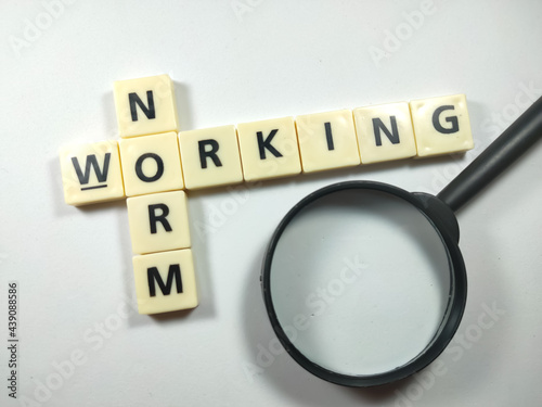 Selective focus.Scrabble letters with text NORM WORKING and magnifying glass on white background.