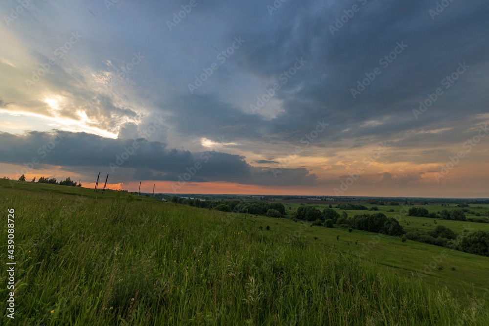 Evening landscape with meadow grasses and clouds above the horizon.