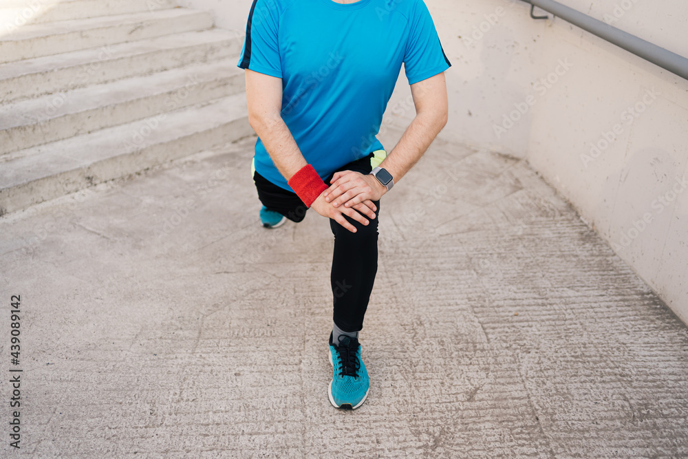 Young man runner getting ready to run stretching legs warm up quad stretch exercise on outdoor staircase