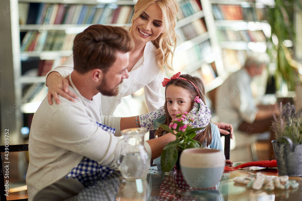 Cheerful parents and their little daughter have a good time while planting at home together. Family, leisure, together Cheerful parents and their little daughter have a good time while planting at home together. Family, leisure, together
