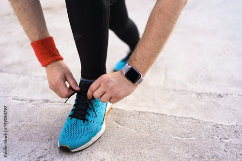 Runner is tying his running shoes. Man shoelace, his blue sneakers with smartwatch on his wrist