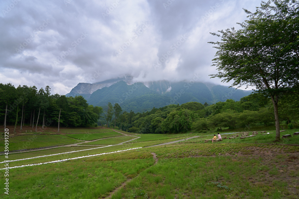 Fototapeta premium Two people relaxing in a field where you can see a mountain covered with clouds