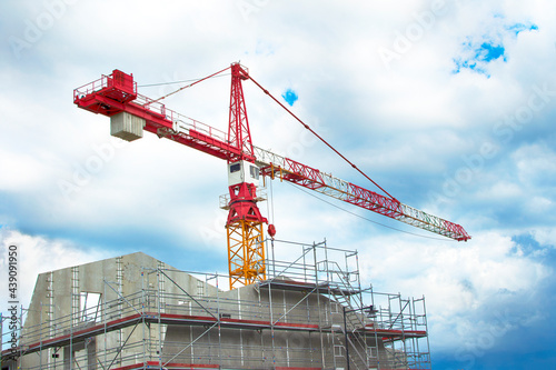 Red construction crane over bulding in progress against blue sky