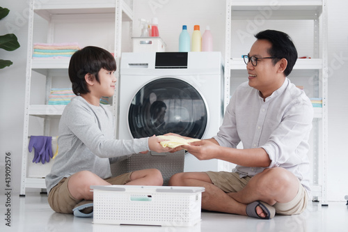 Smiling Asian father and little boy child is enjoying and Washing clothes together in Laundry room on holiday. Family activities and child educational for homeschool concept.
