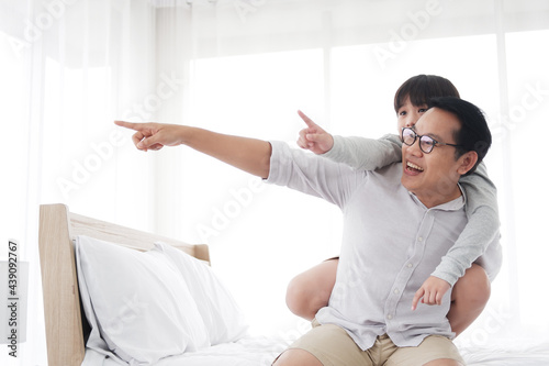 Smiling Asian cute little boy is relaxing and playful with father in bedroom at home. Family love and child educational for homeschool on holiday concept. Focuc at asian boy. photo