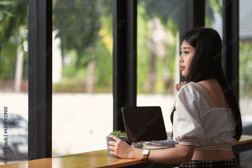 Portrait of young asian businesswoman with glasses holding mug and working with tablet computer while sitting at office desk. Portrait of young asian businesswoman with glasses holding mug and working with tablet computer while sitting at office desk.