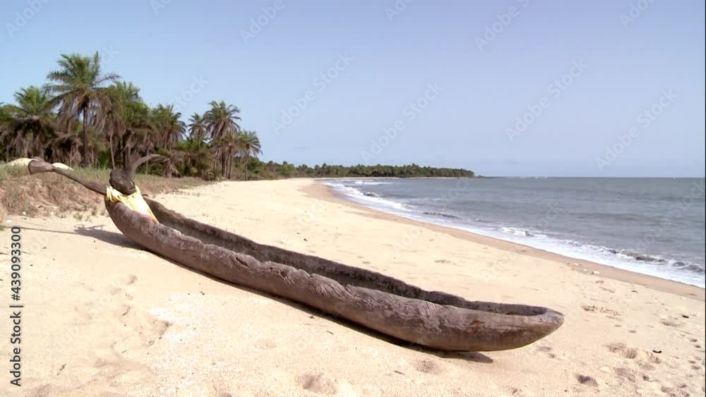 A dugout canoe with a wooden human figure on the beautiful sandy shore of the Atlantic Ocean. Behind the palm grove. A dugout canoe with a wooden human figure on the beautiful sandy shore of the Atlantic Ocean. Behind the palm grove.