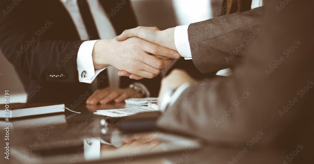 Fototapeta premium Unknown businessman shaking hands with his colleague or partner above the glass desk in modern office, close-up. Business people group at meeting