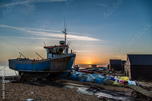 A fishing boat on the beach at sunset surrounded by equipment. Taken on Hythe Beach, Kent, UK photo