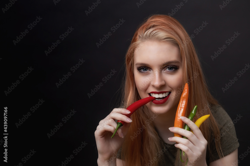 Attractive young woman with red lips is tasting multicolored chili peppers Attractive young woman with red lips is tasting multicolored chili peppers