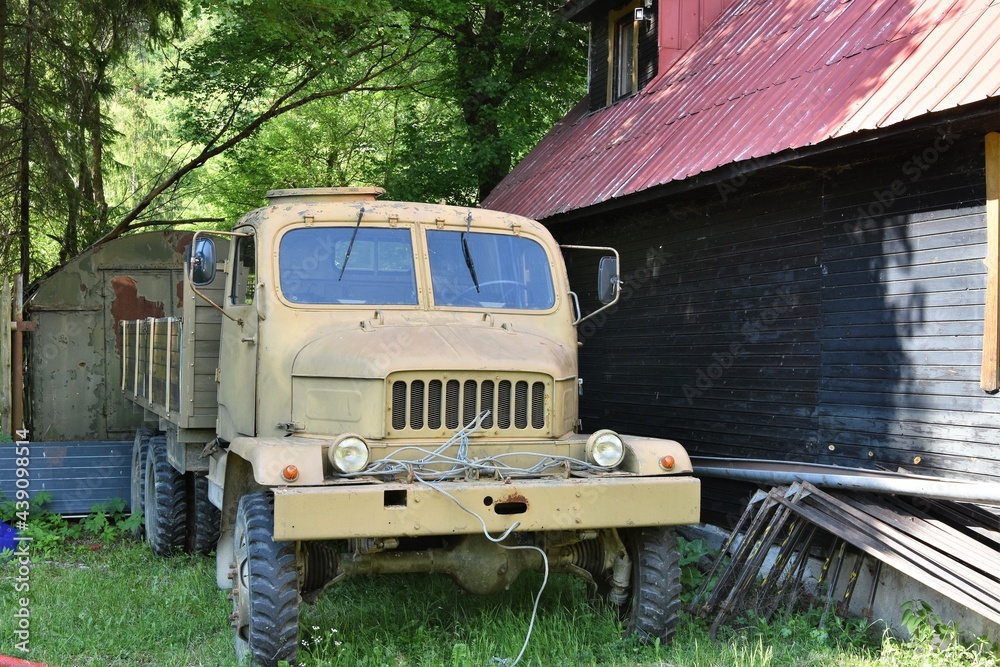 An old all-terrain multi-purpose truck the Praga V3S, produced since 1953 in Czechoslovakia, abandoned in the countryside near village house and green bushes and trees. 