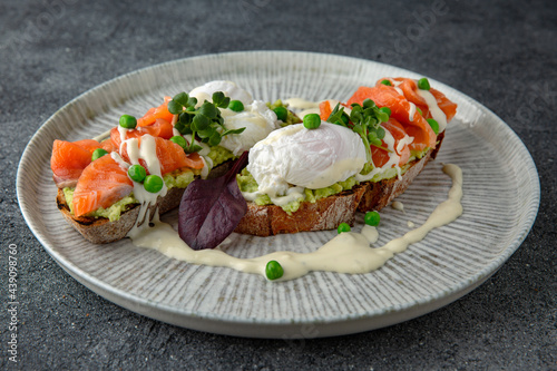 Whole wheat bruschetta with fresh salmon, guacamole, poached eggs and green peas. Ready menu for the restaurant. Neutral gray blue textured background.