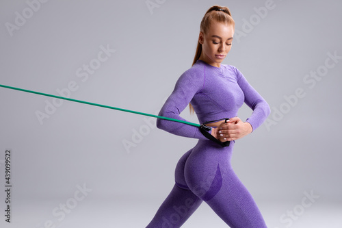 Fitness woman working out with resistance band on gray background. Athletic girl exercises with expander