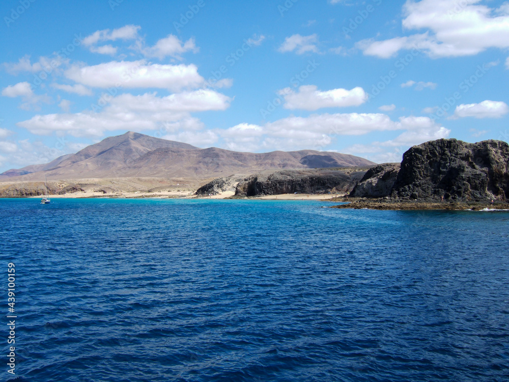 View of a bay with big sandy beach and many bathers between some rocks with deep blue sea on Lanzarote