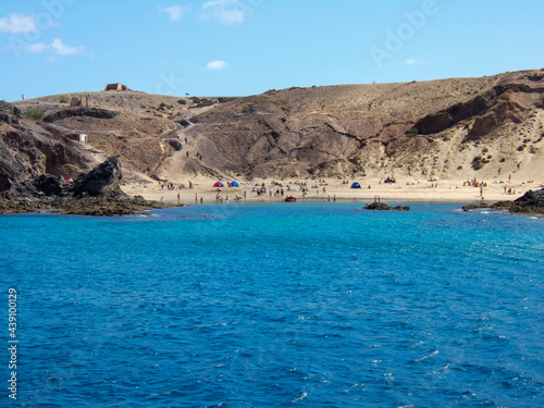 View of a bay with big sandy beach and many bathers between some rocks with deep blue sea on Lanzarote