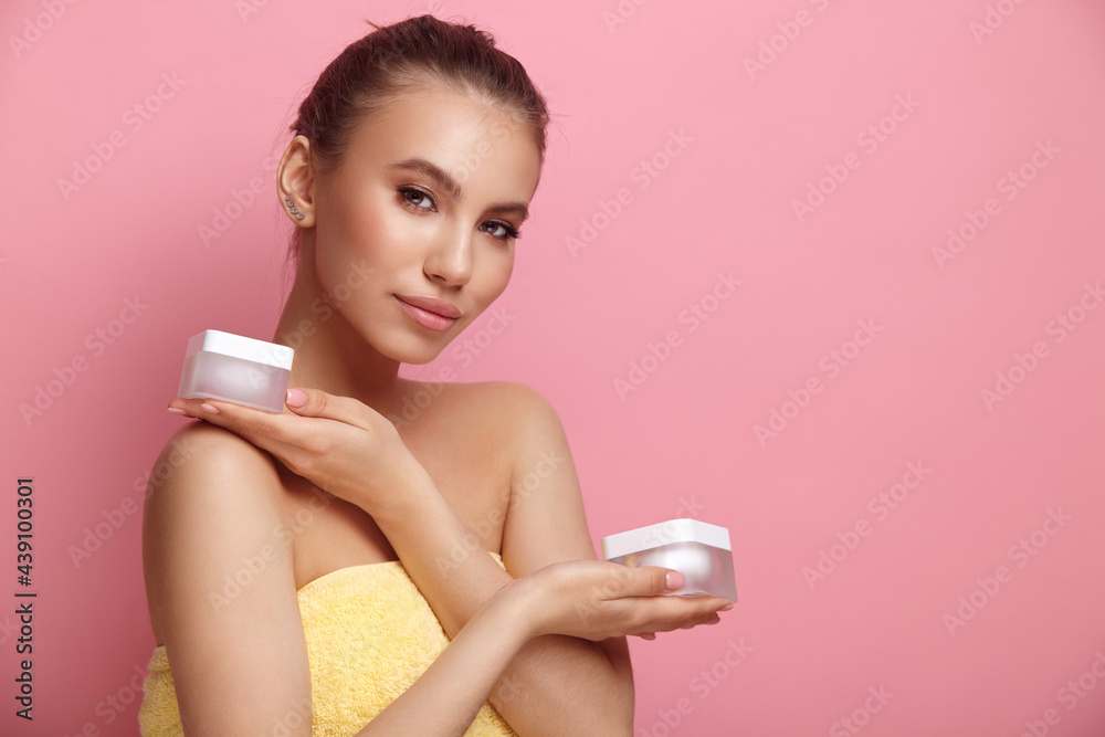 Attractive woung woman with towel holds lotion on pink background Attractive woung woman with towel holds lotion on pink background