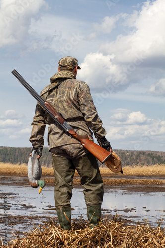 hunter with a duck decoys in both hands stands in front of the swamp photo