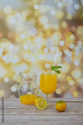 Orange juice in a glass decorated with mint leaves and lemon slices with a pitcher on a wooden table with bokeh background. photo