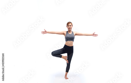 Young woman in grey sport wears doing yoga on leg in studio white background. Concept of home exercise. Yoga time at home.