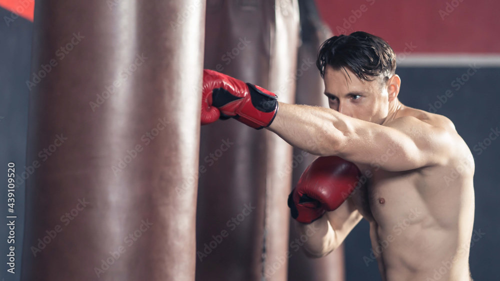 Caucasian boxer shirtless hit a punching bag or boxing Sandbag in gym.