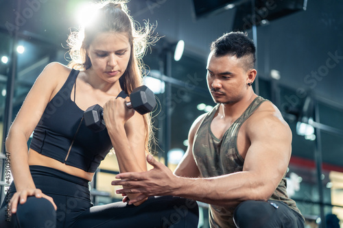 Obraz na plátně Asian Fitness trainer support sportswoman workout lift dumbbell in gym