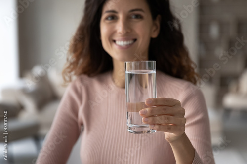 Close up portrait of smiling millennial Hispanic woman recommend drinking clean still mineral water for body refreshment. Happy young Latino female enjoy pure clear aqua. Hydration, habit concept.