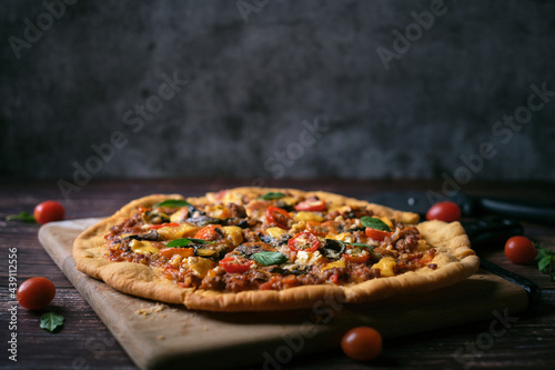 Fresh baked thin crust Italian pizza with tomato sauce pepper cheese and basil leaf on Dark rustic table background.
