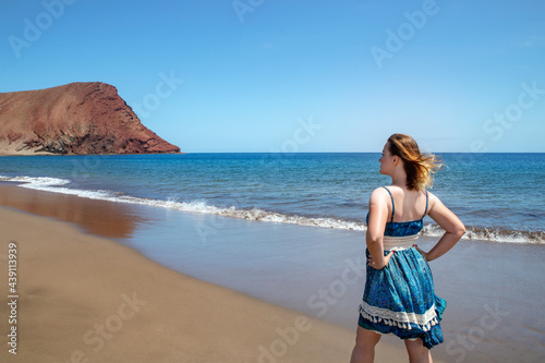 Profile or rear view of a beautiful millennial woman looking towards Playa La Tejita and the volcanic mountain, Montana Roja, and enjoying a sunny but windy summer day, Tenerife, Canary Islands, Spain