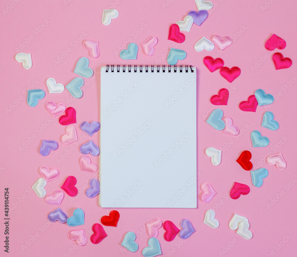 An open blank notebook on a pink background with hearts.