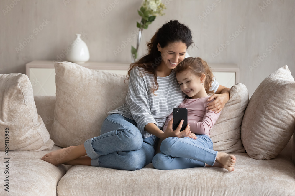 Smiling Latin mother and teen ethnic daughter relax on sofa at home talk speak on video call on smartphone. Happy Hispanic mom and biracial girl child have fun use cellphone have webcam event. Smiling Latin mother and teen ethnic daughter relax on sofa at home talk speak on video call on smartphone. Happy Hispanic mom and biracial girl child have fun use cellphone have webcam event.