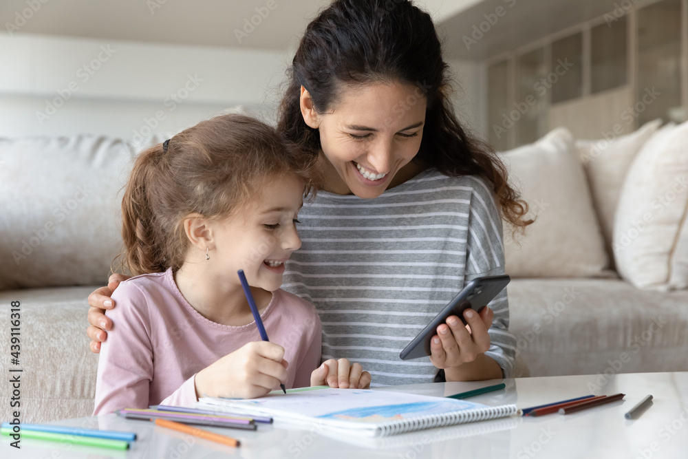 Smiling Hispanic mother and small biracial daughter have fun drawing using modern smartphone gadget. Happy Latino mom and ethnic girl child enjoy painting have online video lesson on cellphone. Smiling Hispanic mother and small biracial daughter have fun drawing using modern smartphone gadget. Happy Latino mom and ethnic girl child enjoy painting have online video lesson on cellphone.