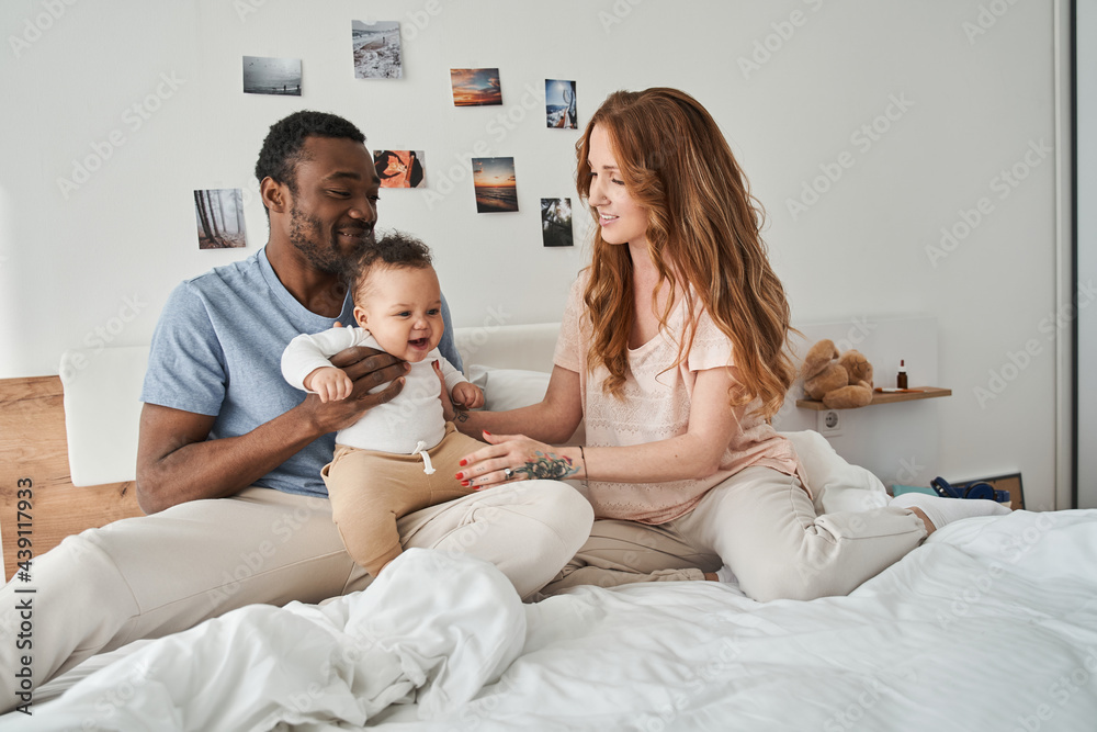Mother, father and their kid hugging and relaxing at the bedroom