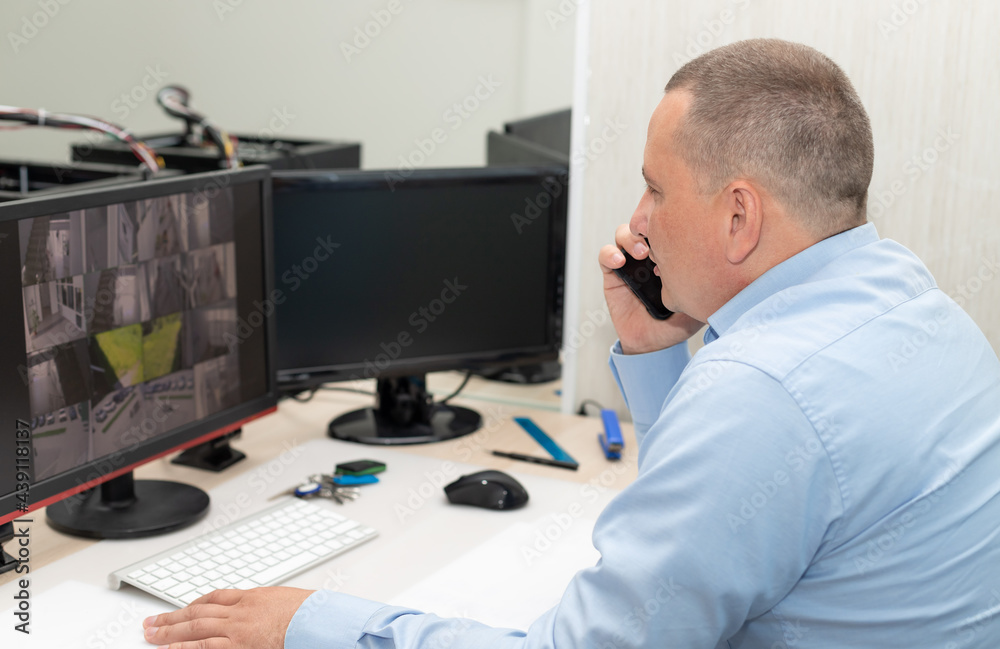 Obraz premium Side view of security guard watching CCTV cameras and talking on mobile phone. Surveillance, control, safety of private property concept. selective focus