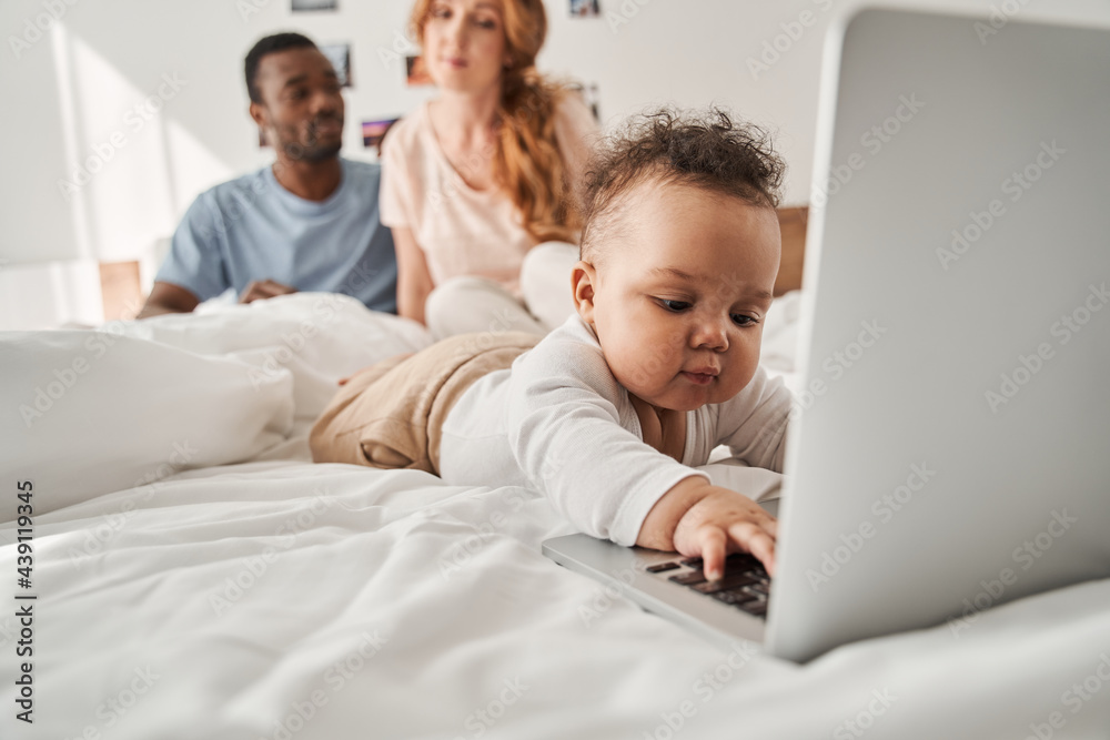 Baby typing at the laptop keyboard while his parents looking at him Baby typing at the laptop keyboard while his parents looking at him