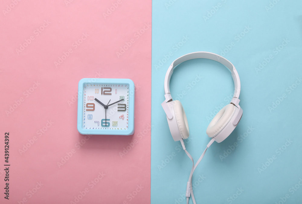 Square alarm clock with headphones on pink blue background. Music time. Top view Square alarm clock with headphones on pink blue background. Music time. Top view