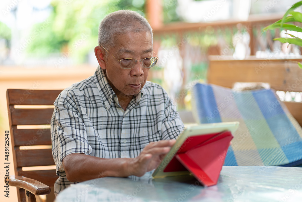 senior asian man using tablet to play social media at home during free time senior asian man using tablet to play social media at home during free time