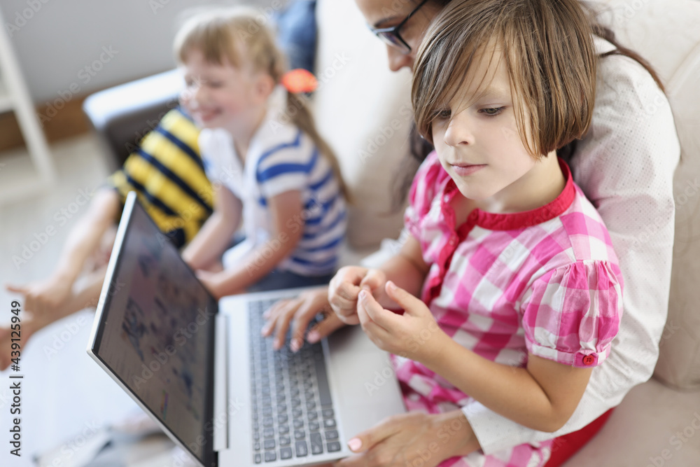 Woman works remotely on laptop on her lap and children are playing nearby Woman works remotely on laptop on her lap and children are playing nearby