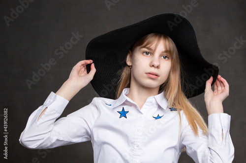 Happy teenage girl in white shirt and black hat is shot against a gray background.