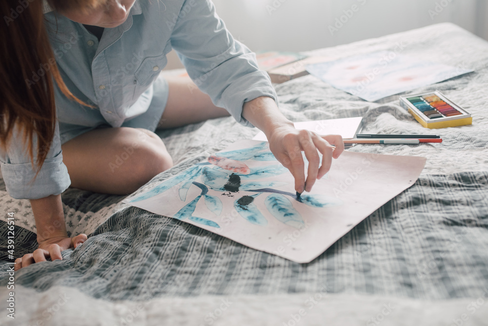 Young woman sitting at the bed and painting at her flat Young woman sitting at the bed and painting at her flat