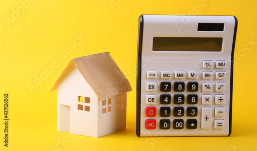 Calculator with paper model of house on yellow background. Calculating cost of housing