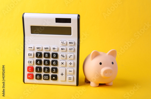 Calculator and piggy bank on yellow background